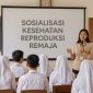 Pemateri berdiri di depan kelas memberikan edukasi kesehatan reproduksi kepada siswa SMA yang duduk berhadapan menghadap layar presentasi.